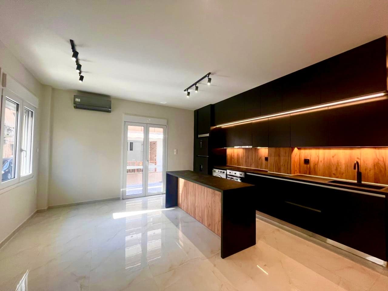 The same room after renovation: open kitchen with black units, breakfast bar and bright stone-effect floor