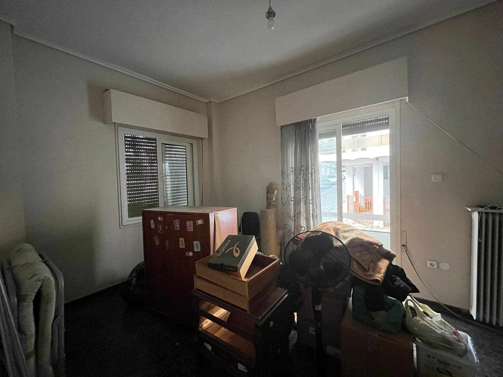 Living room before renovation, dark and used for storage, with a window, balcony door and old radiator