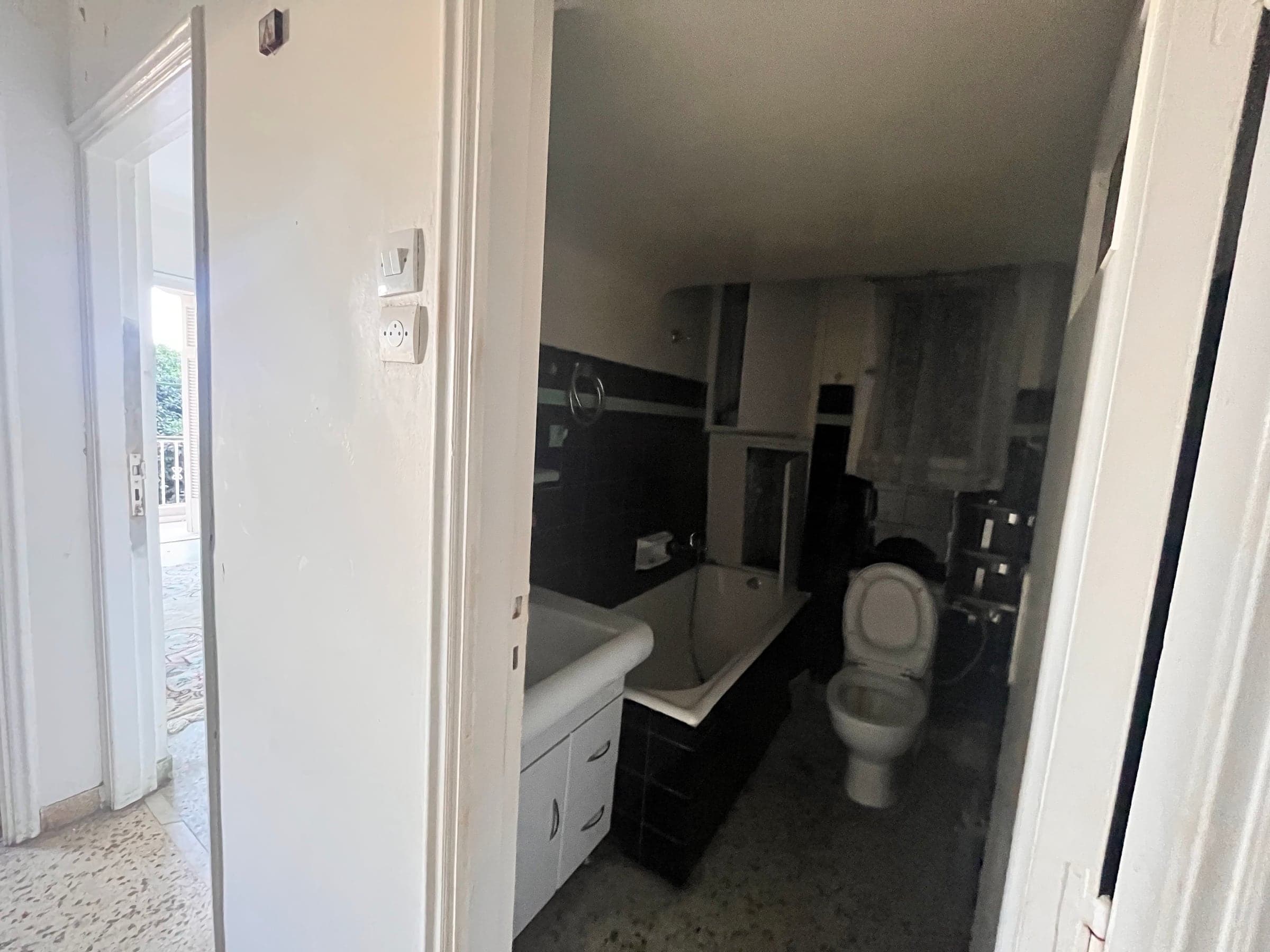 Bathroom before renovation with dark tiles and a built-in bathtub