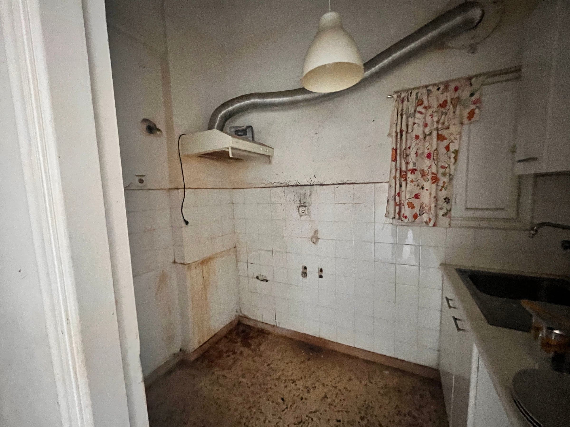 Small enclosed kitchen before renovation with old white tiles and an exposed extractor duct