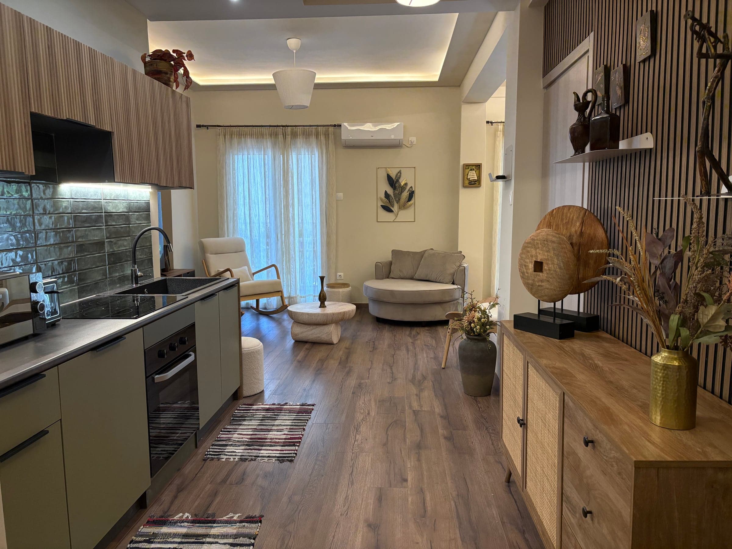The same living room after renovation, now open to a fitted kitchen, with a slatted timber wall and concealed ceiling lighting