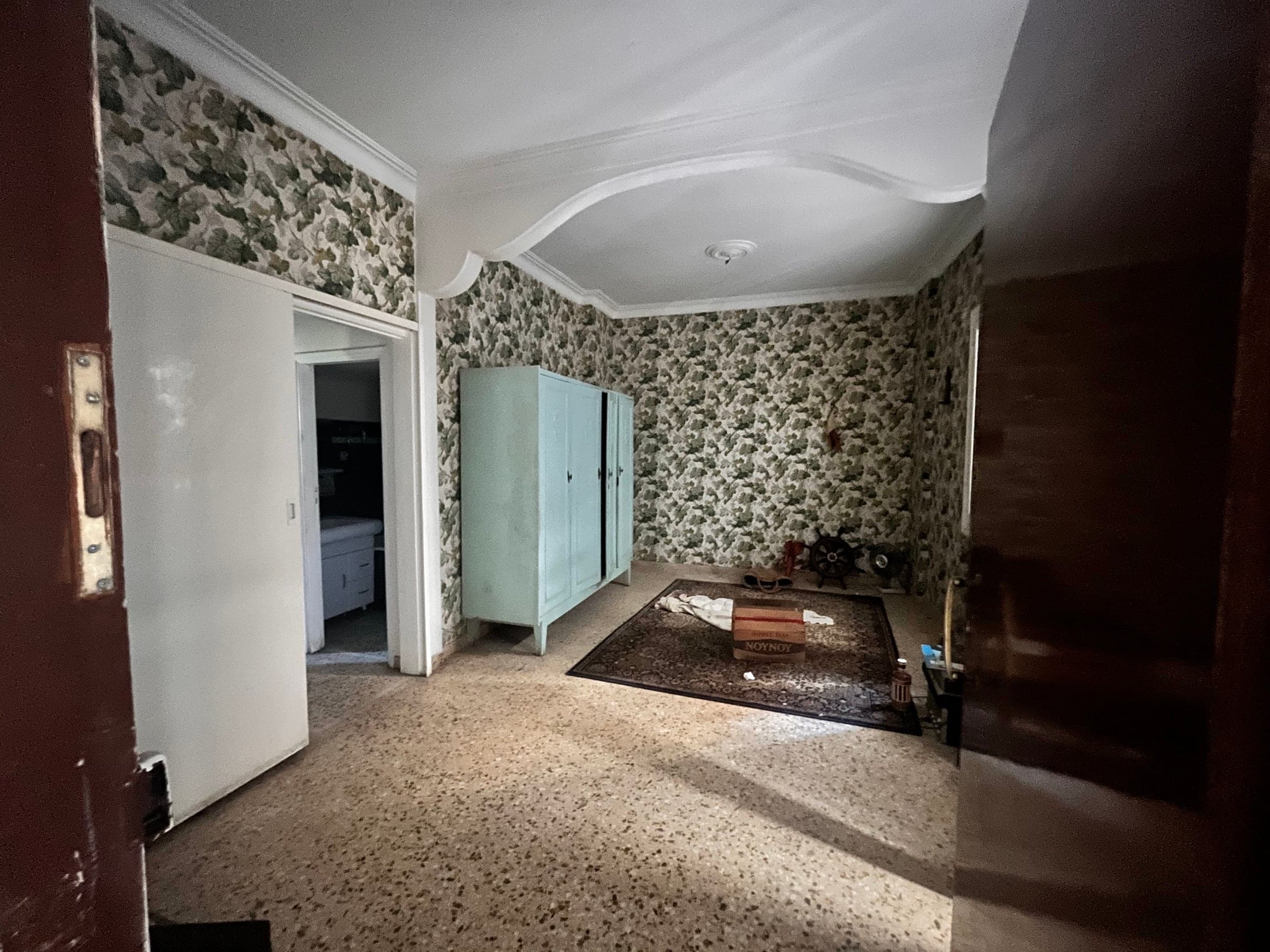Living room before renovation, seen from the entrance, with green patterned wallpaper and mosaic floor